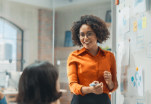 Building Unicorns: 3 Keys to Successful Entrepreneurship A woman standing in front of a white board talking to teammates sitting at a table.