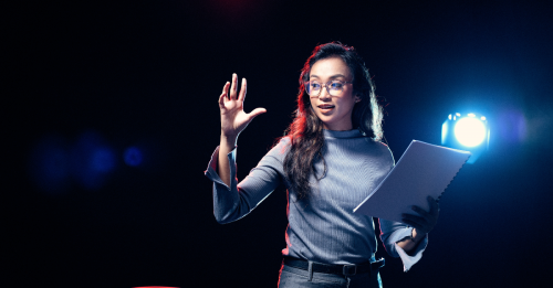 Woman leadership speaker delivering a speech on stage with back lighting