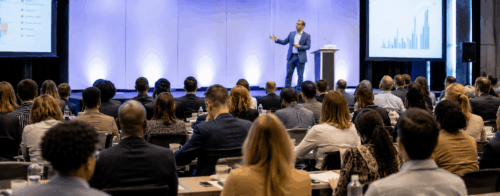 Professional event setting with engaged audience listening to a speaker on stage, representing the high stakes and importance of speaker selection and customization.